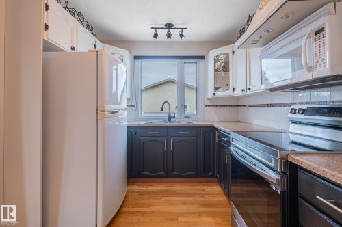 Kitchen featuring light wood-finish flooring, white upper cabinetry, and dark lower cabinetry - 11415 142 Avenue, Edmonton, AB 