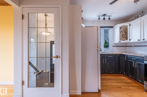 Kitchen featuring wood-finish flooring, two-tone cabinetry with white upper and dark lower cabinets, light-toned countertops, and a white tile backsplash - 11415 142 Avenue, Edmonton, AB 