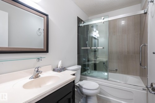 Bathroom featuring a vanity with an integrated sink, a framed mirror, and a glass-enclosed shower/tub combination - 11415 142 Avenue, Edmonton, AB 