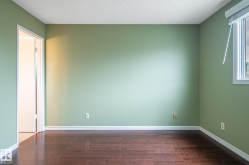Room featuring wood-finish flooring, light green walls, a white trim package, and a window with a white frame - 11415 142 Avenue, Edmonton, AB 