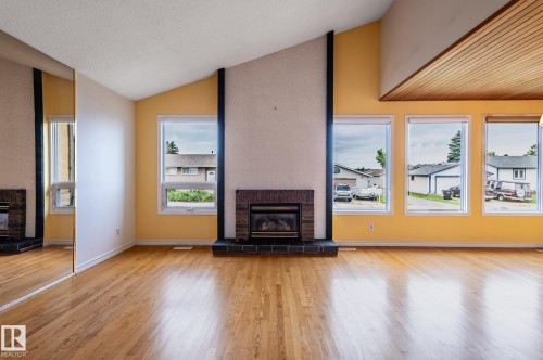 Living area featuring wood-finish flooring, a brick fireplace with a hearth, multiple windows, a mirrored wall, and a wood-paneled ceiling accent - 11415 142 Avenue, Edmonton, AB 
