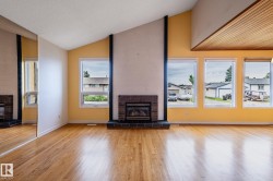 Living area featuring wood-finish flooring, a brick fireplace with a hearth, multiple windows, a mirrored wall, and a wood-paneled ceiling accent - 