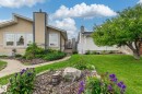 Exterior featuring tan stucco siding, an angled roofline, multiple windows, a prominent chimney, and a landscaped front yard with a manicured lawn and mature trees - 11415 142 Avenue Nw, Edmonton, AB 