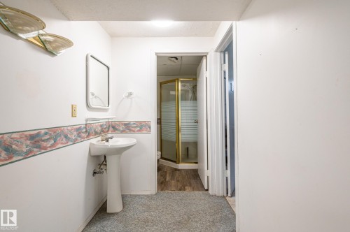 Bathroom featuring a pedestal sink, wall-mounted mirror, and a corner shower with a gold-toned frame and frosted glass panels - 11415 142 Avenue, Edmonton, AB 