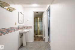 Bathroom featuring a pedestal sink, wall-mounted mirror, and a corner shower with a gold-toned frame and frosted glass panels - 