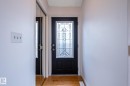 Entryway featuring a black door with decorative glass, wood-finish flooring, and a mirrored closet door - 11415 142 Avenue Nw, Edmonton, AB 