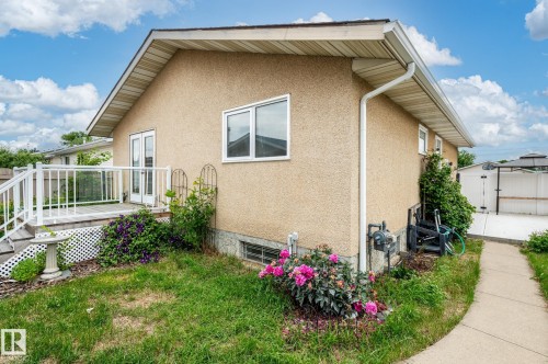 Stucco exterior featuring a wooden deck with white railings, a concrete walkway, and established landscaping - 11415 142 Avenue, Edmonton, AB 