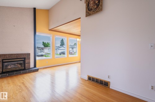 Spacious interior featuring wood-finish flooring, a brick fireplace with a black hearth, and multiple windows - 11415 142 Avenue, Edmonton, AB 