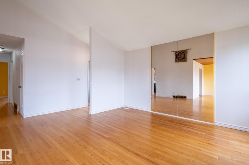 Spacious interior featuring wood-finish flooring, white walls, and a full-height mirrored accent wall - 11415 142 Avenue, Edmonton, AB 