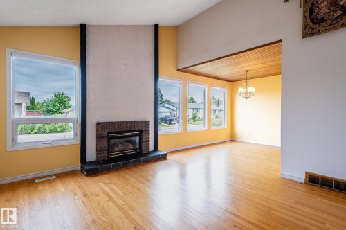 Living area featuring hardwood flooring, a fireplace with brick and tile surround, multiple windows, a vaulted ceiling, and a wood-paneled ceiling section with a chandelier - 11415 142 Avenue, Edmonton, AB 