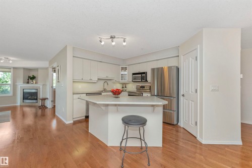 Bright kitchen featuring white cabinetry, stainless steel appliances, a center island with countertop seating, and wood-finish flooring - 130 9008 99 Avenue Nw, Edmonton, AB 