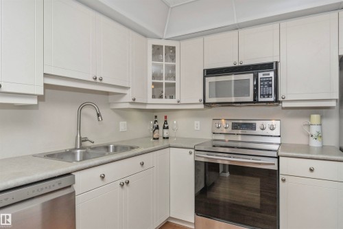 Kitchen featuring white cabinetry, a stainless steel double basin sink with pull-down faucet, a built-in microwave, a stainless steel electric range, and a stainless steel dishwasher - 130 9008 99 Avenue Nw, Edmonton, AB 