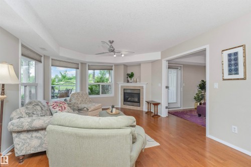 Living area featuring wood-finish flooring, a corner fireplace with tile surround, and multiple windows with roller shades - 130 9008 99 Avenue Nw, Edmonton, AB 