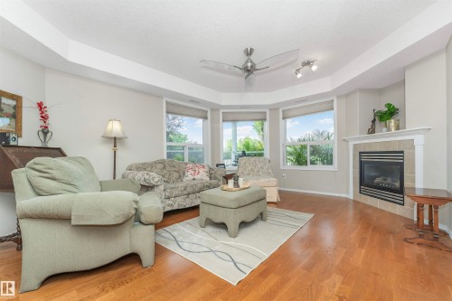 Living area with wood-finish flooring, a corner fireplace featuring a tile surround and mantel, and a bay window configuration - 130 9008 99 Avenue Nw, Edmonton, AB 