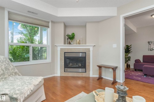 Corner fireplace with a tile surround and white mantel, complemented by wood-finish flooring - 130 9008 99 Avenue Nw, Edmonton, AB 