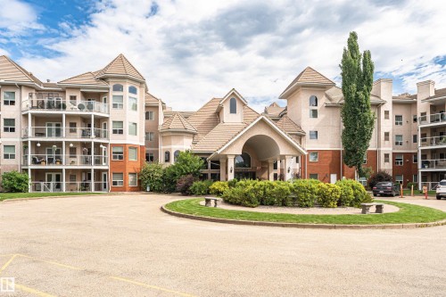 Multi-level stucco and brick exterior featuring a grand covered entrance, multiple private balconies with glass railings, and a prominent turret architectural element - 130 9008 99 Avenue Nw, Edmonton, AB 