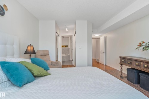 Spacious bedroom featuring light-toned walls, wood-finish flooring, recessed lighting, and a white paneled headboard - 130 9008 99 Avenue Nw, Edmonton, AB 