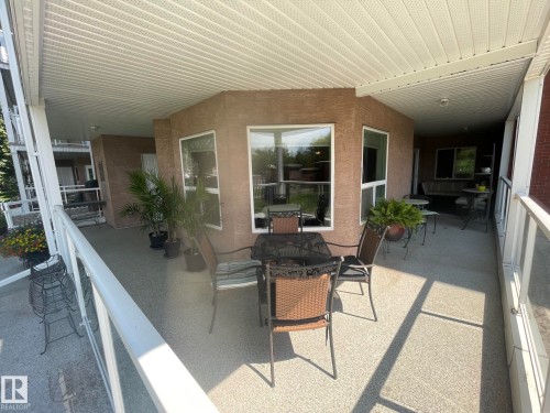 Expansive outdoor patio featuring a speckled concrete surface, white railing, and a durable soffit ceiling - 130 9008 99 Avenue Nw, Edmonton, AB 