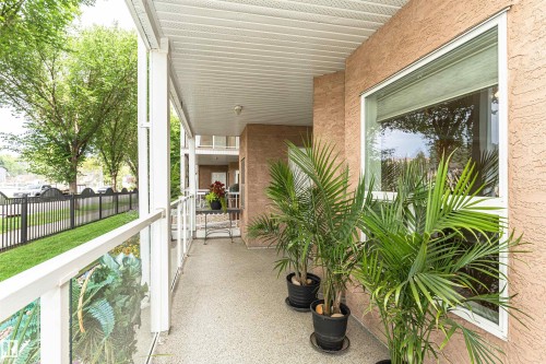 Expansive covered balcony featuring a textured stucco exterior, white window trim, and durable flooring - 130 9008 99 Avenue Nw, Edmonton, AB 