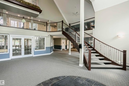 Two-story foyer featuring a grand staircase with dark wood-finish handrails and decorative metal balusters - 130 9008 99 Avenue Nw, Edmonton, AB 