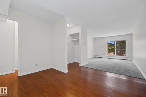 Expansive dining and living room featuring rich wood-finish flooring transitioning to plush gray carpeting - #6E 11608 28 Av Nw Nw, Edmonton, AB - Indoor Photo Showing Other Room