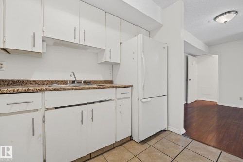 Kitchen featuring white cabinetry, a stainless steel sink, and a speckled countertop - #6E 11608 28 Av Nw Nw, Edmonton, AB - Indoor Photo Showing Kitchen