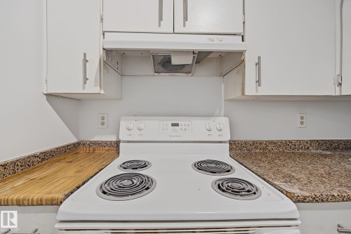 Kitchen featuring a white electric range with four coil burners, white cabinetry with brushed nickel hardware, a white range hood, and speckled countertops - #6E 11608 28 Av Nw Nw, Edmonton, AB - Indoor Photo Showing Kitchen