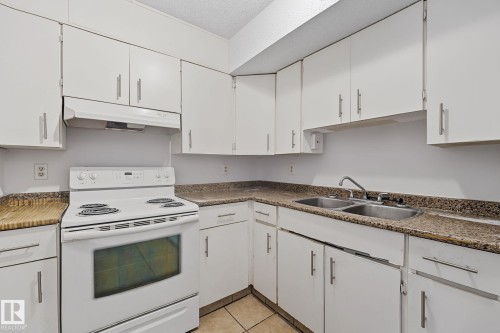 Kitchen featuring white cabinetry, speckled countertops, a double basin stainless steel sink, and a white electric range with a coordinating range hood - #6E 11608 28 Av Nw Nw, Edmonton, AB - Indoor Photo Showing Kitchen With Double Sink