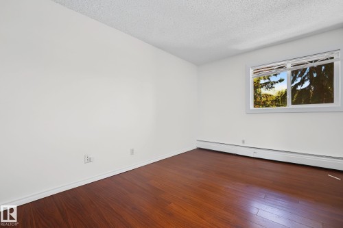 Spacious room featuring rich wood-finish flooring, crisp white walls, and a large window - #6E 11608 28 Av Nw Nw, Edmonton, AB - Indoor Photo Showing Other Room