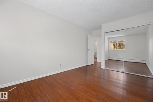 Spacious room featuring wood-finish flooring, white walls, and bright baseboards - #6E 11608 28 Av Nw Nw, Edmonton, AB - Indoor Photo Showing Other Room