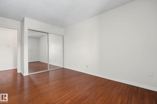 Room featuring wood-finish flooring, white baseboards, and a mirrored sliding closet door - #6E 11608 28 Av Nw Nw, Edmonton, AB - Indoor Photo Showing Other Room