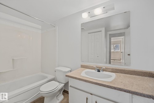 Bathroom featuring a bathtub with an integrated shower, a white toilet, a vanity with an integrated sink, a light-colored countertop, and a wall-mounted mirror with overhead lighting - #6E 11608 28 Av Nw Nw, Edmonton, AB - Indoor Photo Showing Bathroom