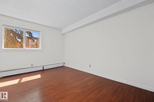 Room featuring wood-finish flooring, white baseboards, and a large window - #6E 11608 28 Av Nw Nw, Edmonton, AB - Indoor Photo Showing Other Room