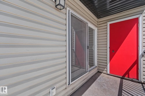 Exterior patio featuring light-colored horizontal siding, a red entry door to storage, and a sliding glass door with screen - #6E 11608 28 Av Nw Nw, Edmonton, AB - Outdoor With Exterior