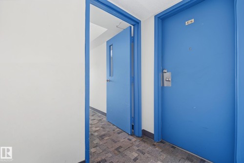 Corridor featuring two blue doors with white trim and a patterned carpet flooring - #6E 11608 28 Av Nw Nw, Edmonton, AB - Indoor Photo Showing Other Room