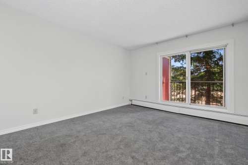 Carpeted interior space featuring white walls and a sliding glass door with balcony access - #6E 11608 28 Av Nw Nw, Edmonton, AB - Indoor Photo Showing Other Room