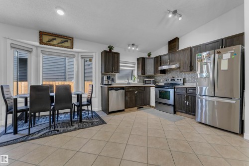 Open-concept kitchen and dining area featuring dark wood-finish cabinetry, stainless steel appliances, and a tiled backsplash - 1316 35 Street, Edmonton, AB 