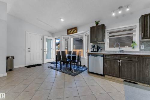 Kitchen with wood-finish cabinetry, stainless steel dishwasher, and a grey mosaic tile backsplash - 1316 35 Street, Edmonton, AB 
