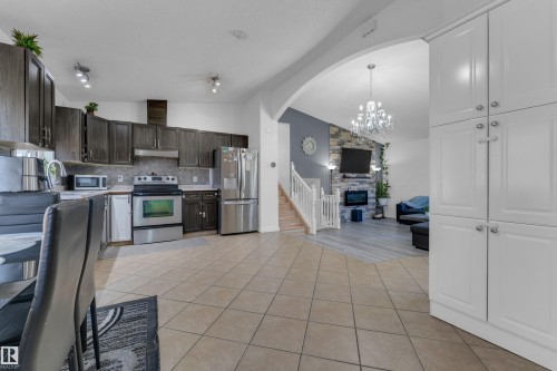 Open-concept living space with a kitchen featuring dark wood-finish cabinetry, stainless steel appliances, and tile flooring - 1316 35 Street, Edmonton, AB 