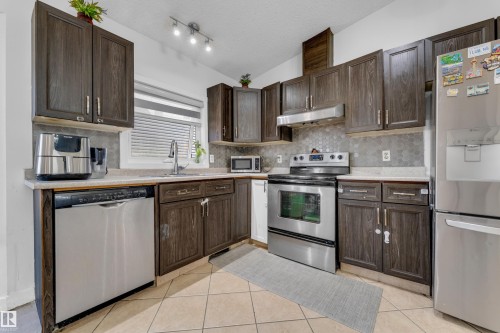 Kitchen featuring wood-finish cabinetry, stainless steel appliances, a hexagon tile backsplash, and light-toned countertops - 1316 35 Street, Edmonton, AB 