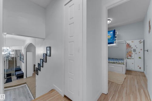 Hallway featuring wood-finish flooring, white paneled doors, and a staircase leading to a lower level with a chandelier - 1316 35 Street, Edmonton, AB 
