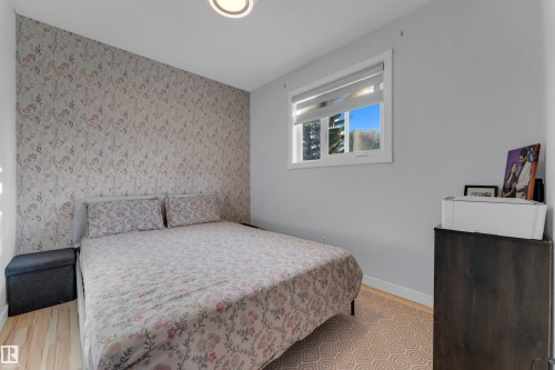 Bedroom featuring a window with white trim, light wood-finish flooring, and a patterned accent wall - 1316 35 Street, Edmonton, AB 
