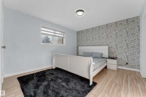 Bedroom featuring wood-finish flooring, a decorative accent wall, a flush-mount ceiling light, and a window with blinds - 1316 35 Street, Edmonton, AB 