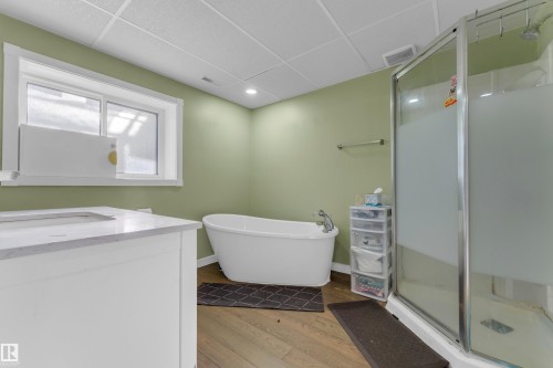 Bathroom featuring a freestanding tub, glass-enclosed shower, single vanity with integrated sink, wood-finish flooring, and a window - 1316 35 Street, Edmonton, AB 