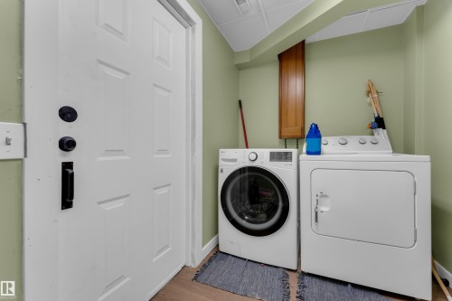 Laundry area featuring wood-finish flooring, light green walls, a white paneled door with black hardware, and an overhead built-in wood cabinet - 1316 35 Street, Edmonton, AB 