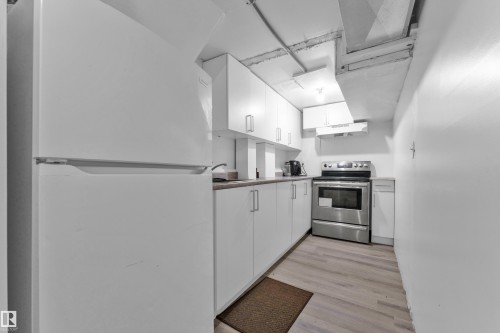 Galley kitchen featuring a white refrigerator, stainless steel range, white cabinetry, light countertops, and wood-finish flooring - 1316 35 Street, Edmonton, AB 