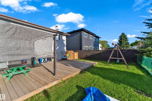 Expansive outdoor living area featuring a large wood deck, a partial sunshade over a portion of the deck, a broad lawn, and a dark privacy fence - 1316 35 Street, Edmonton, AB 