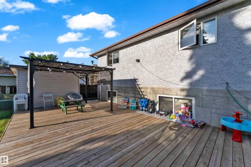 Expansive wood deck with a black metal pergola, stucco siding, and a basement window - 1316 35 Street, Edmonton, AB 