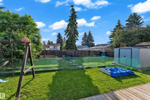Expansive backyard featuring a manicured lawn, established trees, a raised wood deck, and a metal storage shed - 1316 35 Street, Edmonton, AB 