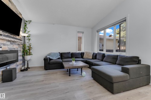 Living area featuring a stone-clad fireplace with a built-in media console, wood-finish flooring, vaulted ceilings, and large windows - 1316 35 Street, Edmonton, AB 